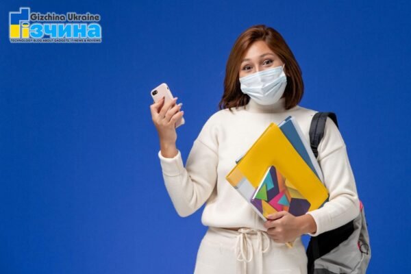 202102front view female student white jersey wearing mask backpack holding phone with headphones blue wall college university book lessons