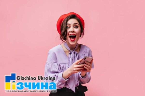 202104emotional woman red beret stylish shirt joyful surprise looks camera holds white smartphone pink background