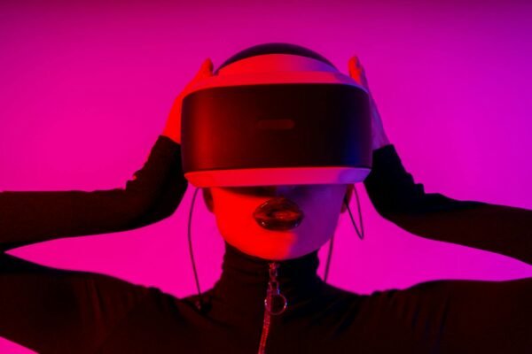 Astonished young female using virtual reality goggles while experiencing invisible reality on pink background